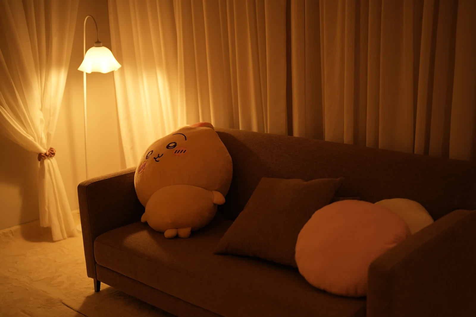 The atelier lounge: sheer curtains, a sofa with cushions and a warm floor lamp